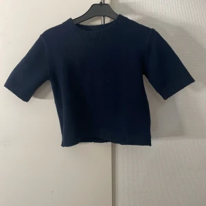 Mörkblå stickad tröja Kappahl - En stilren mörkblå stickad tröja från Kappahl med korta ärmar och ribbade muddar vid hals, ärmslut och nederkant. Perfekt för dig som gillar enkel och klassisk stil. Passar till många olika outfits och är superenkel att matcha.