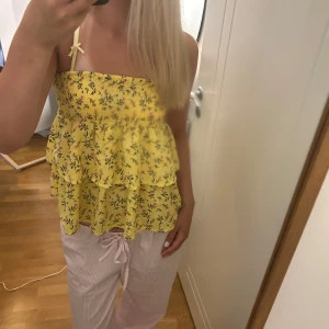 Gul blommig volangtop med smock - Supersöt gul topp med blommigt mönster och volanger ,Smockad upptill . Perfekt för varma dagar och ger en riktigt somrig vibe. Luftig och lätt, passar till både jeans och kjol.kan även användas som kjol.
