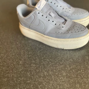Nike Air Force 1 i ljus blå skinn - Snygga Nike Air Force 1 sneakers i ljus blå färg . Skorna har perforerad tå, rund tå och tydlig Nike-logga på sidan och hälen. Perfekt för dig som gillar stilrena och tidlösa sneakers med lite chunky vibe.     Men…. Skorna saknar sko snören tyvärr men annars är dom rätt så fräscha använts några fåtal gånger 4 ish 