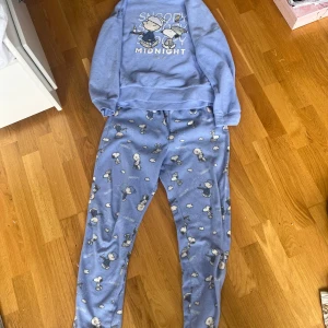 Blå fleecebyxor med Snoopy från Peanuts - Mysiga blå fleecebyxor med Snoopy-tryck från Peanuts. Byxorna har ett gulligt mönster med Snoopy och små moln över hela tyget. Perfekta för chill dagar hemma när du vill vara extra bekväm.