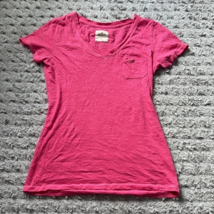 Rosa v-ringad t-shirt från Hollister - Snygg rosa t-shirt från Hollister i v-ringad modell. T-shirten har korta ärmar, liten bröstficka med broderad logga och är gjord i mjuk bomull!💕