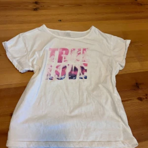 Somrig t-shirt/topp - Vit t-shirt med korta ärmar och rund halringing. Framsidan har ett fint tryck i rosa och blå toner med texten True love. Fin och somrig och går lätt att styla med en kjol eller ett par jeans. Fint skick, nästan som ny! (Strl 158-164, men passar bra på mig som har S)