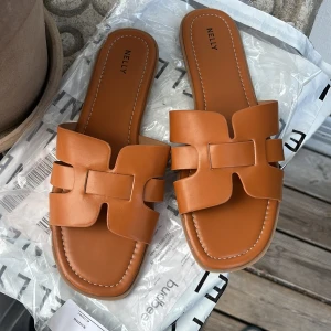 Bruna slip-in sandaler från Nelly - Stolek 40 , Aldrig använda har förpackning och allt kvar !        Slut sålda överallt Snygga slip-in sandaler från Nelly i en varm brun cognac-nyans. De har breda remmar i skinnimitation med coolt utskuret mönster och platt sula. Perfekta för sommardagar och lätta att matcha med allt.