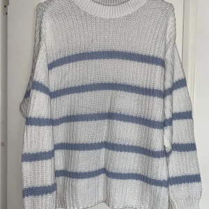 Vit stickad tröja med blå ränder - Vit stickad tröja med breda ljusblå ränder och rund hals. Tröjan har en avslappnad passform och långa ärmar. 