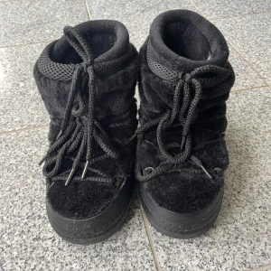Svarta boots med snörning - Mysiga svarta boots med fluffig pälsimitation och grova snören framtill. Skorna har rund tå och platt sula, perfekt för kalla vinterdagar. Insidan är vadderad för extra komfort och värme. Använda 2ggr!