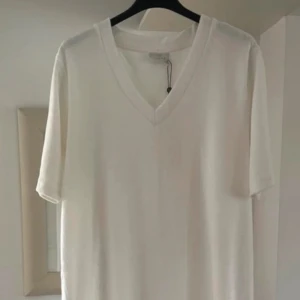 Vit v-ringad frotté klänning från Kaffe - Vit frotté klänning från Kaffe med v-ringning och korta ärmar. Enkel och clean design i mjuk bomullsblandning, perfekt för en chill och stilren look. Materialet är 80% bomull och 20% polyester. 