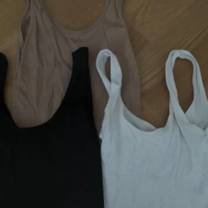 Tre ribbade linnen i basfärger - Tre stilrena ribbade linnen i svart, beige och vitt. Alla är ärmlösa med breda axelband och rundad halsringning. Perfekta att matcha med jeans eller kjol för en enkel och snygg look.