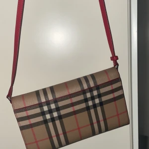 Burberry rutig axelväska i skinn - Säljer en snygg axelväska från Burberry i klassiskt rutig design med beige, svart och röda toner. Den är äkta köpt i NK Göteborg för ungefär 5 år sedan för 7000ish. Använd 2-3 gånger aldrig mer den är i jätte gott skick dock har jag tappat bort kvittot till den . 