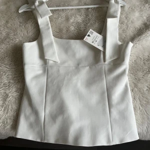 Vit linnetopp med rosettband från Zara - Supersnygg vit linnetopp från Zara med breda axelband som knyts i rosetter. Toppen har en rak, något figurnära passform. Inte mina bilder och prislappen är inte kvar men den är bara använd en gång💞