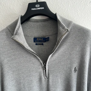 Grå half zip tröja Polo Ralph Lauren - Snygg grå tröja från Polo Ralph Lauren i mjuk pima bomull. Modellen har half zip-dragkedja, ribbad krage och diskret broderad logga på bröstet. Perfekt för lager-på-lager och chill stil. Passar både till jeans och chinos.