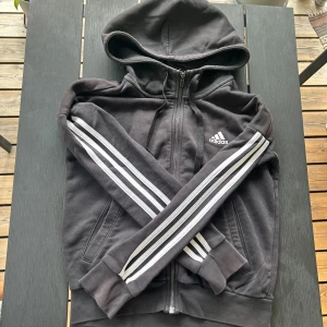 Svart Adidas zip hoodie - Svart hoodie från Adidas i XS med klassiska vita ränder längs ärmarna 🖤 väldigt snygg ”croppad” passform