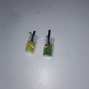 Örhängen i form av små flaskor - Unika örhängen som ser ut som små glasflaskor med sugrör. Ena flaskan har gul och vit vätska, den andra grön och gul. Perfekt för dig som gillar roliga och annorlunda accessoarer.