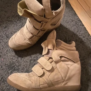 Beiga kilklackade sneakers i mocka - Snygga beiga sneakers med kilklack och coola detaljer. Skorna är gjorda i mocka och har tre breda kardborreband framtill. Nästan identiska till Isabel marant skon! 