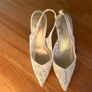 Vita spetsiga pumps från ASOS Design - Snygga vita pumps med spetsig tå och hög klack från ASOS Design. Skorna har ett romantiskt blommigt spetsmönster och öppen häl med smal rem. Perfekta för dig som vill sticka ut med en elegant och feminin look. Det står storlek 40 i men passar mig som har 38. Sparsamt använda
