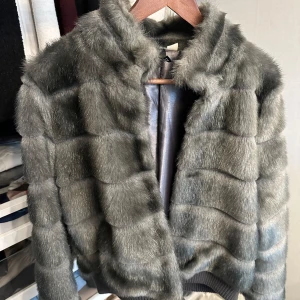 Grå pälsjacka i storlek 42 - Säljer en fluffig och lyxig grå pälsjacka med snyggt rutmönster. Jackan har en kortare modell och är helfodrad med silkeslen insida. Perfekt för dig som vill sticka ut och hålla dig varm med stil. Passar till både jeans och klänning.