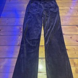 Bruna  velourbyxor Juicy Couture - Bruna velourbyxor från Juicy Couture med bred resår i midjan, snörning och två stora bakfickor med knappar. Broderad JC-logga framtill. Använda ett par fåtal gånger.