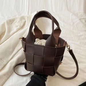 Brun flätad axelväska i skinn - Snygg brun axelväska med flätad design och justerbar axelrem. Väskan har två rejäla handtag och är tillverkad i skinn. Perfekt storlek för det viktigaste och ger en trendig touch till din outfit.