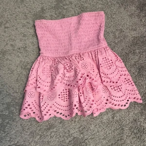 Rosa bandeau tubtopp med volang - Supersöt rosa bandeau tubtopp från Stradivarius med broderade hålmönster och volangkant. Smockad upptill för perfekt passform och luftig känsla. 