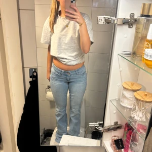 Ljusblå bootcut jeans med broderi - Säljer ett par ljusblå jeans med bootcut-modell och snyggt rött broderi på bakfickorna. Jeansen har låg midja och klassisk femficksdesign. Perfekta för dig som gillar en avslappnad men ändå trendig look.