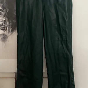 Mörkgröna skinnbyxor från Bik Bok - Snygga mörkgröna byxor i skinnimitation från Bik Bok. Modellen har raka ben, klassisk femficksdesign och knappstängning i midjan. 