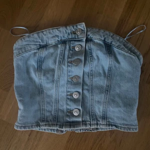 Ljusblå jeans tubtopp från Zara - Snygg ljusblå tubtopp i jeans från Zara med knappar framtill och smockad rygg för extra passform. Toppen har tunna avtagbara axelband. Aldrig använd då den är för liten. 