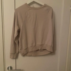 Beige sweatshirt från H&M Basics - Enkel och stilren beige sweatshirt från H&M Basics i storlek S. Tröjan har rund halsringning, långa ärmar och en något längre bakdel. Perfekt för en chill och avslappnad look.