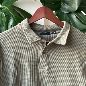 Beige pikétröja i bomull från 157 - Säljer en beige pikétröja från 157 i skön, grovstickad bomull. Tröjan har klassisk krage, korta ärmar och knäppning framtill med två knappar. Perfekt för dig som gillar en avslappnad men ändå stilren look.