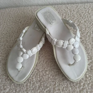 Nya, vita sandaler med pärldetaljer - Snygga vita sandaler med fyrkantig tå och låg klack. Remmarna är dekorerade med vita pärlliknande detaljer som ger en cool och somrig vibe. Perfekta för varma dagar och lätta att matcha med olika outfits.