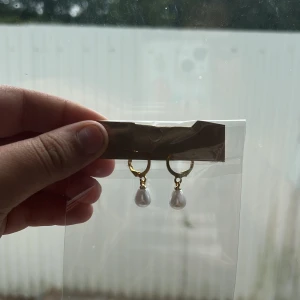 Guldiga örhängen med pärlor - Snygga örhängen med guldfärgade ringar och droppformade vita pärlor som hänger ner. Perfekta för att ge din look en elegant touch. Passar dig som gillar klassiska smycken med en modern twist.