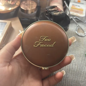 Too Faced Chocolate Matte Bronzer - Säljer en Too Faced Chocolate Matte bronzer i en snygg rund guldig dosa med spegel. Pudret är matt och har en varm brun nyans, perfekt för att ge ansiktet en solkysst look. Lyxig förpackning med chokladdoft.