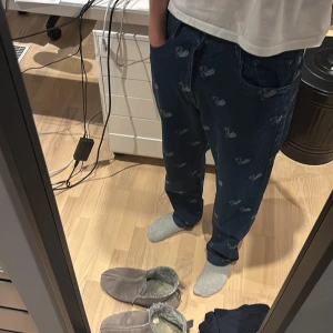 Blå jeans med svanmönster Skagen M - Unika blå jeans från Skagen Clothing i storlek M, dekorerade med broderade svanar över hela byxan. Klassisk femficksmodell med rak passform och normal midja. Tillverkade i jeansmaterial som känns både slitstarkt och bekvämt.