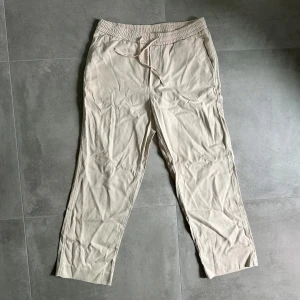 Beiga byxor från A Day's March - Snygga beiga byxor från A Day's March i 100% tencel. De har elastisk midja med dragsko och raka ben. Perfekta för en chill och stilren look, med fickor fram och en bakficka. Lätta och sköna att bära hela dagen. Artnr:A330