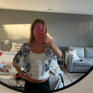 Vit och blå blommig bolerotopp - Säljer en superfin bolerotopp i tunn,  blått blommönster. Toppen har korta, vida ärmar och öppen front som ger en chill och somrig vibe. Perfekt att slänga över ett linne eller klänning för en extra touch. Sytt om själv.