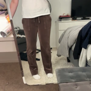 Bruna velourbyxor Juicy Couture S - Mysiga bruna velourbyxor från Juicy Couture med raka ben, snörning i midjan och stora fickor både fram och bak. Perfekta för chill dagar och har en klassisk 00-talsvibe. Mjukt material och snygg passform. Har tyvärr tappat en knapp där bak och tappat änden av ena snöret.