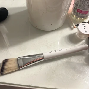 Ansiktsmask borste från Rituals vit - Säljer en ansiktsmask från Rituals med vitt handtag och silverfärgat fäste. Borsten har täta, ljusa strån med mörka toppar och är perfekt för applicering av ansiktsmask eller foundation. Snygg och stilren design som passar på varje sminkbord. Knappt använd 💕