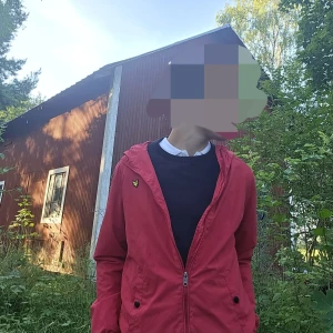 Röd vindjacka från Lyle & Scott - Snygg röd vindjacka från Lyle & Scott med klassisk gul logga på bröstet. Jackan har dragkedja framtill, huva och en clean look som passar perfekt till streetwear. Materialet är lätt och smidigt, perfekt för blåsiga dagar.riktigt fet