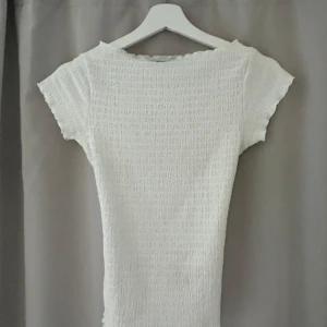 Vit omlottopp från BikBok XS - Supersöt vit topp från BikBok i storlek XS. Den har en smockad struktur, korta ärmar och en  rygg med knytband. Perfekt för dig som gillar en feminin och trendig stil. Toppens material känns lätt och passar bra till varma dagar. Storlek Xs. Aldrig använd. 💕💕💕