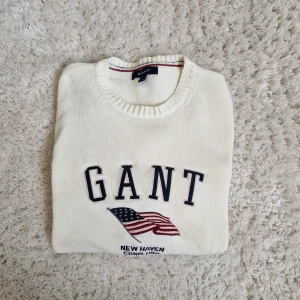 Vit stickad tröja från GANT - Snygg vit stickad tröja från GANT med broderad amerikansk flagga och texten GANT på bröstet. Tröjan är nästan aldrig använd. 
