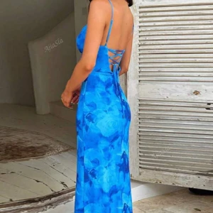 Blå långklänning med snörning i ryggen - Snygg långklänning i blått med blommigt mönster och tunna axelband. Klänningen har en figurnära passform och öppen rygg med snörningsdetalj. Perfekt för sommarens alla tillfällen när du vill sticka ut lite extra.