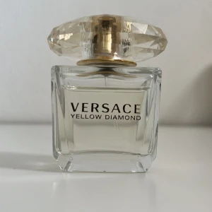 Versace Yellow Diamond parfym - Versace Yellow Diamond är en lyxig parfym i en transparent glasflaska med en stor, diamantformad gul kork. Flaskan har eleganta linjer och guldiga detaljer som ger en exklusiv känsla. Doften är fräsch och feminin, perfekt för dig som gillar eleganta och fruktiga toner.
