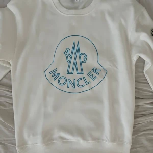 Vit sweatshirt från Moncler med blå logga - !OBS! Det är storlek m men den är liten i storleken så skulle mer säga att den är storlek s!