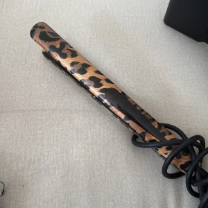 Plattång med leopardmönster - Cool plattång med leopardmönster i brunt och svart. Smal design med svarta keramiska plattor och knappar på sidan för enkel användning. Perfekt för att styla håret med extra attityd. Sladd medföljer. 100-240 v