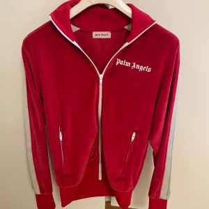 Röd velourjacka från Palm Angels - Palm Angels chenille red velourjacka med vita detaljer och dragkedja framtill. Jackan har vita ränder längs ärmarna, hög krage och två fickor med dragkedja. Ikonisk logga på bröstet. Tillverkas inte längre! (ÄKTA) pris kan diskuteras vid snabb affär, billigaste där ute.
