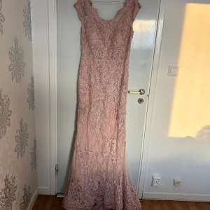 Lång rosa spetsklänning med pärlor - Superfin långklänning i ljusrosa spets med massor av broderade detaljer och pärlor. Klänningen har en elegant, figurnära passform och är ärmlös. Perfekt för bal eller fest, med vacker släp och exklusiv känsla. Använt den 1 gång, nypris 6000kr men går att diskutera vid snabb affär 