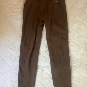 Bruna ribbade leggings från Aim'n - Säljer ett par bruna ribbade leggings från Aim'n. De är högmidjade och har en tight passform med stretchigt material som sitter skönt. Perfekta för träning eller chill. Snyggt diskret Aim'n-märke framtill och ribbad struktur hela vägen.helt nya aldrig använt 