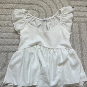 Vit volangblus från lager 157, stl S - Supersöt vit blus från 157 i storlek S. Den har volangärmar, v-ringning och en flowy, rynkad nederdel. Tyget är lätt strukturerat och känns luftigt, perfekt för varmare dagar. Enkel att styla med jeans eller kjol. Är klippt där bak pga att den var för lång för mig.