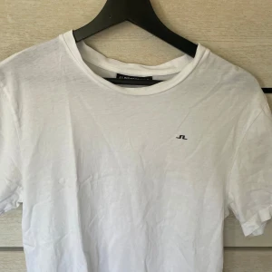 Vit t-shirt från J.Lindeberg - Klassisk vit t-shirt från J.Lindeberg med liten svart logga på bröstet. Lite skrynklig men enbart använd ett fåtal gånger passar S/M 