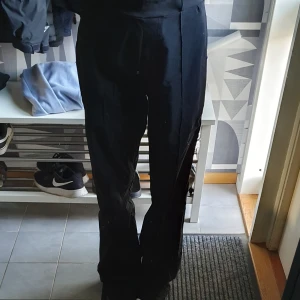 Svarta kostymbyxor med raka ben - Säljer ett par svarta kostymbyxor med hög midja och raka ben. Byxorna har klassisk passform och är perfekta för en clean och stilren look. Materialet känns mjukt och följsamt, och de har pressveck framtill för en extra dressad känsla.