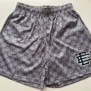 Gråmönstrade shorts med logga M - Snygga grå shorts med rutigt mönster och elastisk midja. De har en stor broderad logga i mörkblått och vitt på ena benet. Perfekta för en chill och trendig look, passar till både t-shirt och hoodie.
