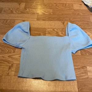 Ljusblå ribbad topp från H&M - Supersöt ljusblå topp från H&M med ribbad struktur och puffiga korta ärmar. Toppen har en rak, croppad passform och fyrkantig halsringning. Perfekt för dig som gillar en enkel men trendig look.